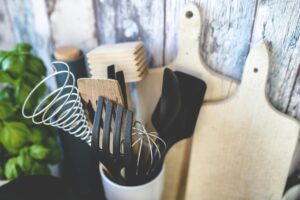 Collection of kitchen utensils including spatula, whisk, and chopping boards against a rustic background.
