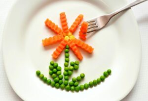 A playful flower made from carrots and peas on a white plate with a fork, showcasing creativity in food art.